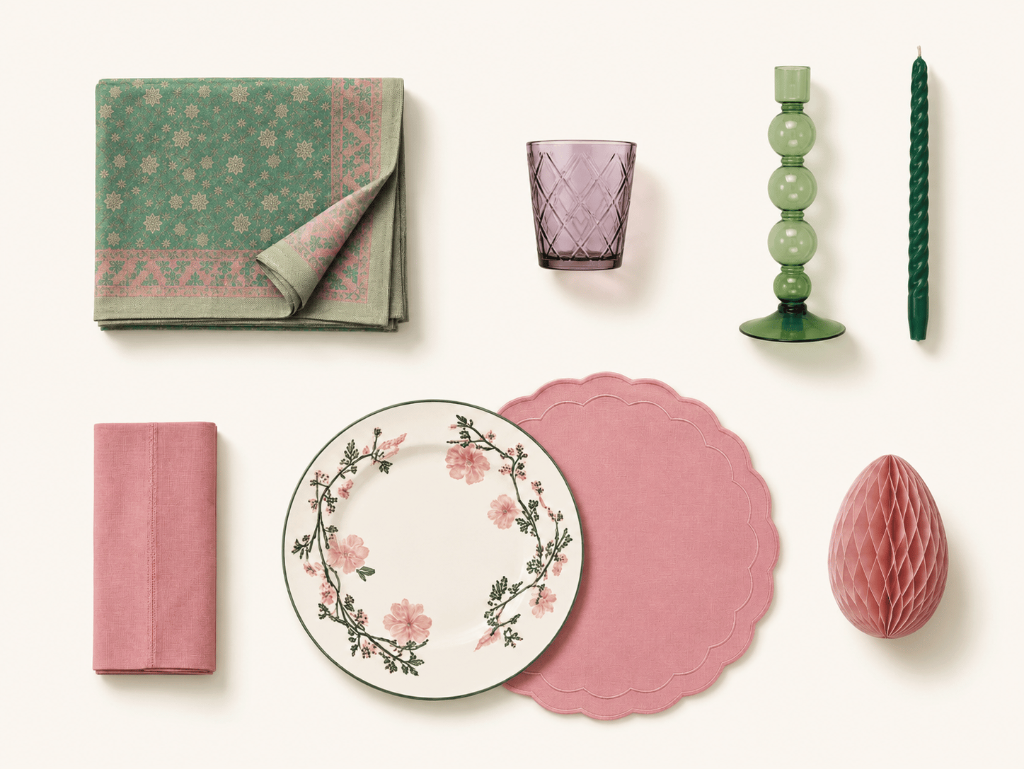 Flat lay of The Celebration set: a folded jacquard tablecloth and pink napkin, a purple cut-glass tumbler, a green bubble candlestick with taper candle, a floral dinner plate on a scalloped pink placemat, and a pink honeycomb decoration.
