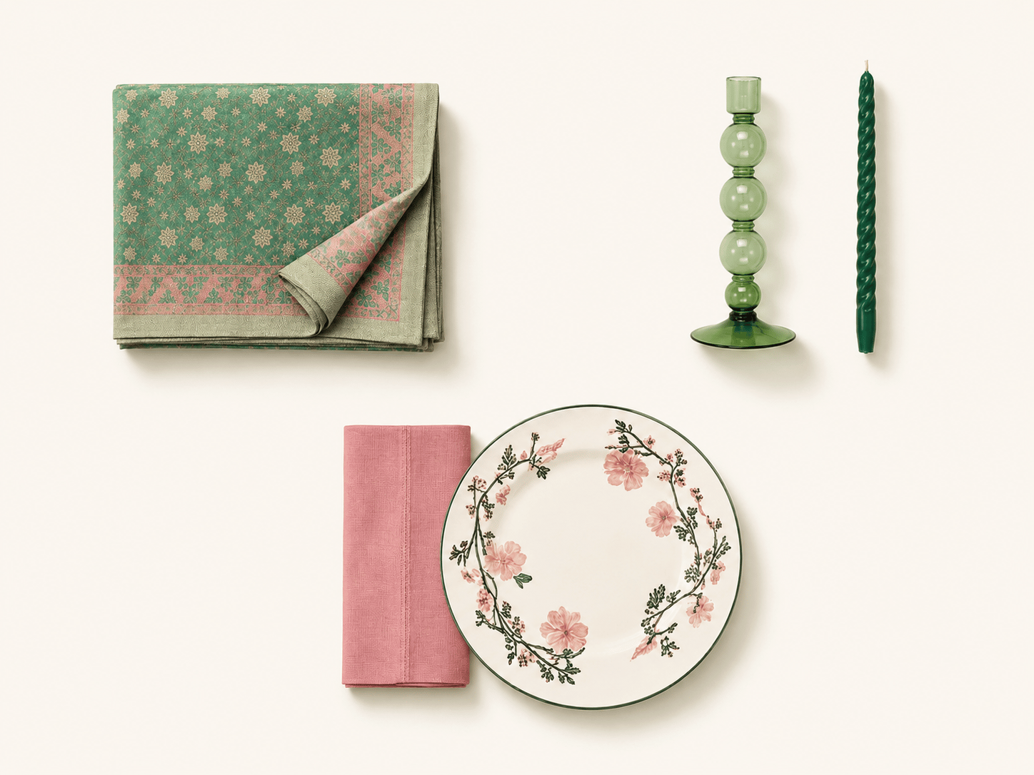 Flat lay of The Gathering set: a folded green and pink jacquard tablecloth, a green bubble candlestick with a twisted taper candle, a floral dinner plate, and a pink linen napkin.