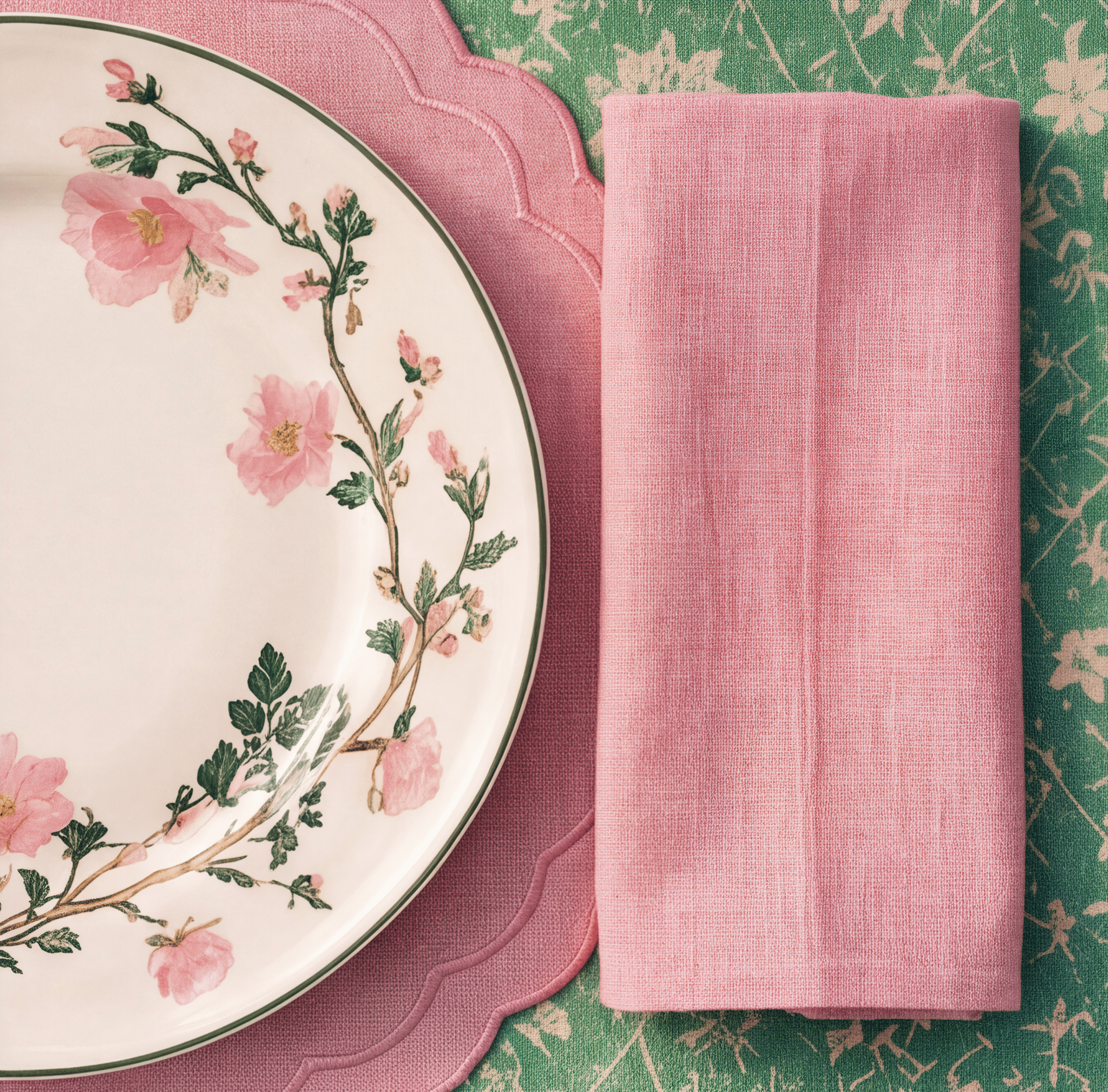 Detail shot of a floral-rimmed plate beside a folded pink linen napkin.